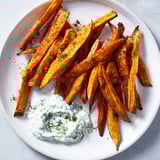 A close-up of crispy sweet potato fries on a baking sheet, ready for serving with yogurt dip.