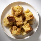 Warm bread pudding with apples and cinnamon, showing soft fruit and a golden baked crust glistening invitingly.