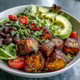 Hearty Sweet Potato and Black Bean Bowl served on greens with fresh salsa and avocado.