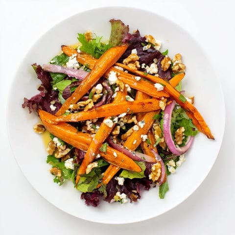 Gelb-orange Karottenbandnudeln liegen auf grünem Salat mit einer glänzenden Honig-Senf-Vinaigrette und zerbröseltem Feta.