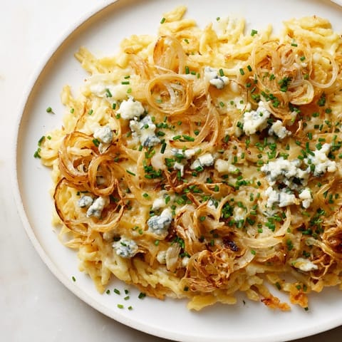 A close-up of Käse-Spätzle Luxus with melted Gorgonzola and caramelized onions, ready to eat.