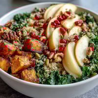 Farbenfroher Kale Harvest Grain Bowl mit gerösteten Süßkartoffeln, saftigen Granatapfelkernen und knusprigen Pepitas auf dem Teller.